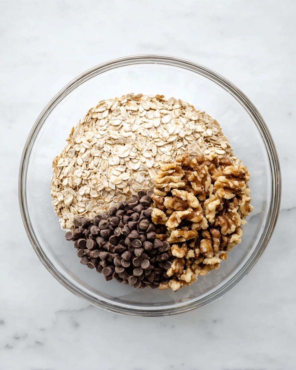 A white plate on a white marbled surface holds six round oatmeal cookies, each with a textured top showing rolled oats and small dark chocolate chips scattered throughout. The cookies vary slightly in size and shape, with uneven edges and a golden-brown color indicating light baking. The oats give each cookie a rough, chunky surface, and the chocolate chips peek out in small dark spots. The arrangement is casual, with cookies spread out but close enough to show a group. photo taken with an iphone --ar 4:5 --v 7